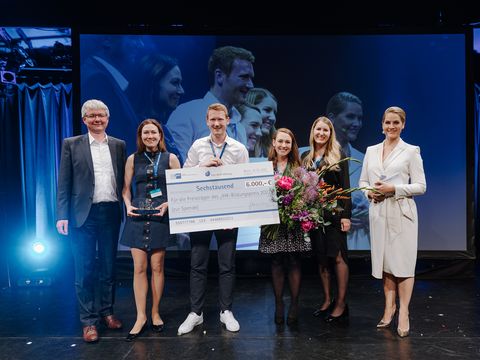 Geschäftsleitung Miriam Häring steht mit fünf weitere Personen auf der Bühne und hält den Bildungspreis 2022 in der Hand