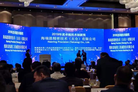 blaue Leinwand mit weißer chinesischer Schrift "2019 - Häring Precision (Taicang) Co., Ltd" vor Bühne sitzen Menschen hören sich den Vortrag an