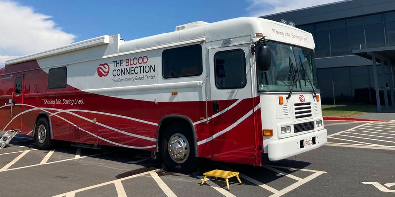 weiß roter Bus mit Schwarz roter Aufschrift "The Blood Connection" auf Parkplatz