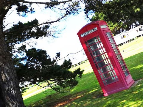 rotes Telefonhäuschen unter einem Baum auf einer Wiese im Hintergrund sind weiße Häuser
