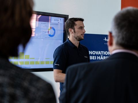 Ein männlicher Mitarbeiter von Häring spricht vor einem Display 