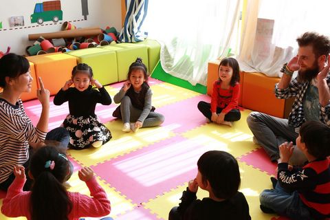 Kindergaren Taicang Erzieher und Kinder sitzen im Kreis auf rot gelben Matten spielen ein Spiel Kindergartenraum