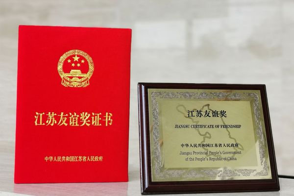 Freundschaftspreise, links rotes kleines Buch mit chinesischer goldener Aufschrift und rechts ein goldenes Bild mit holz Umrandung und schwarzer Schrift "Jiangsu Certificate of Friendship - Jiangsu Provincial People´s Government of the People´s Republic of China"