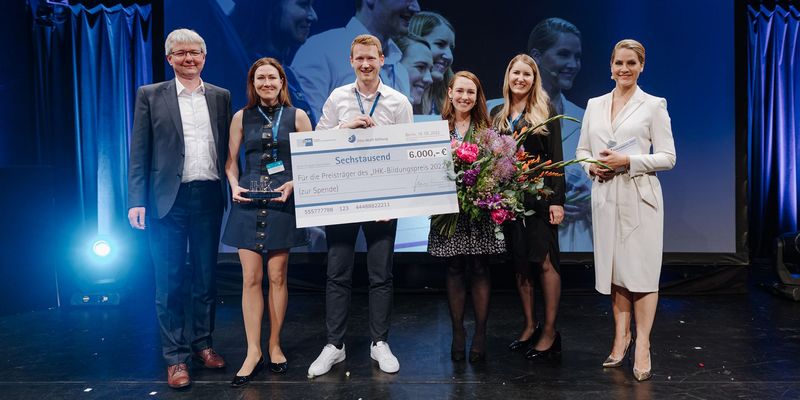 Geschäftsleitung Miriam Häring steht mit fünf weitere Personen auf der Bühne und hält den Bildungspreis 2022 in der Hand