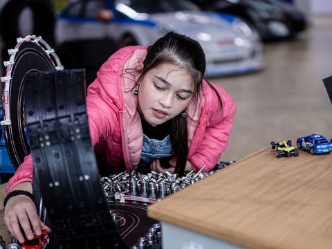 junges dunkelhaariges Mädchen spielt an einer Carrera Rennbahn